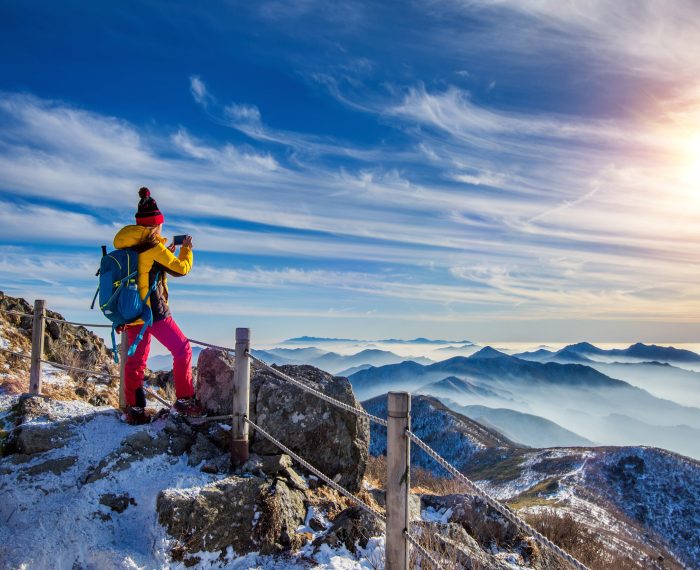 Young woman hiker taking photo with smartphone on mountains peak in winter.